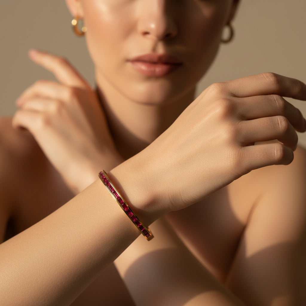 A model's wrist wearing the Ruby Line Gold Bangle to demonstrate its vibrant color and elegant, structured fit.