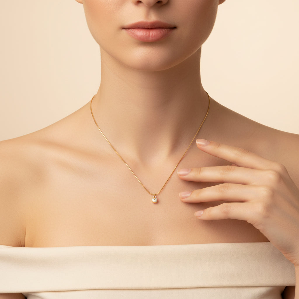 An appealing lifestyle photograph of a model in a pose with her hand, showcasing the cushion-cut solitaire bezel pendant necklace under dramatic lighting against a minimal, light background.