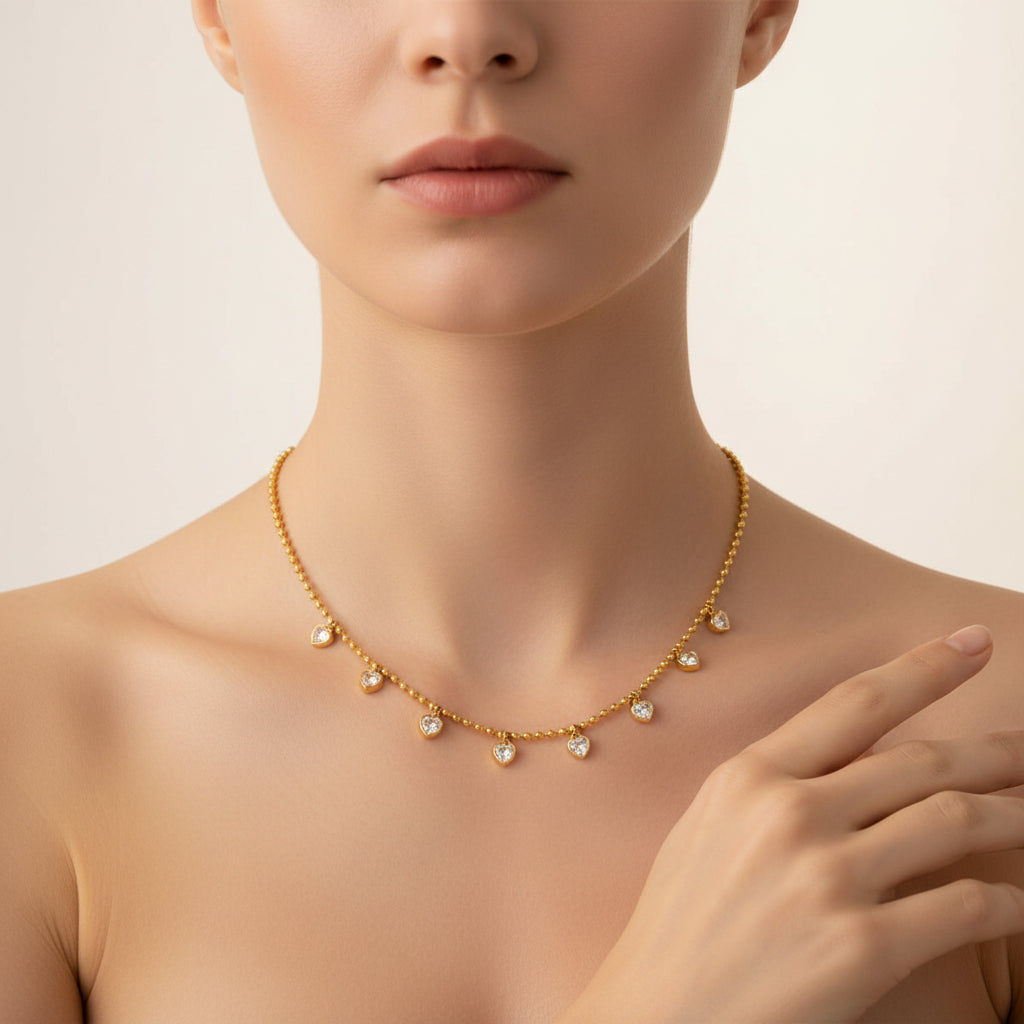 An appealing lifestyle photograph of a model in a full body pose with her hand, highlighting the cascading gold heart crystal station chain necklace under dramatic lighting against a minimal background.