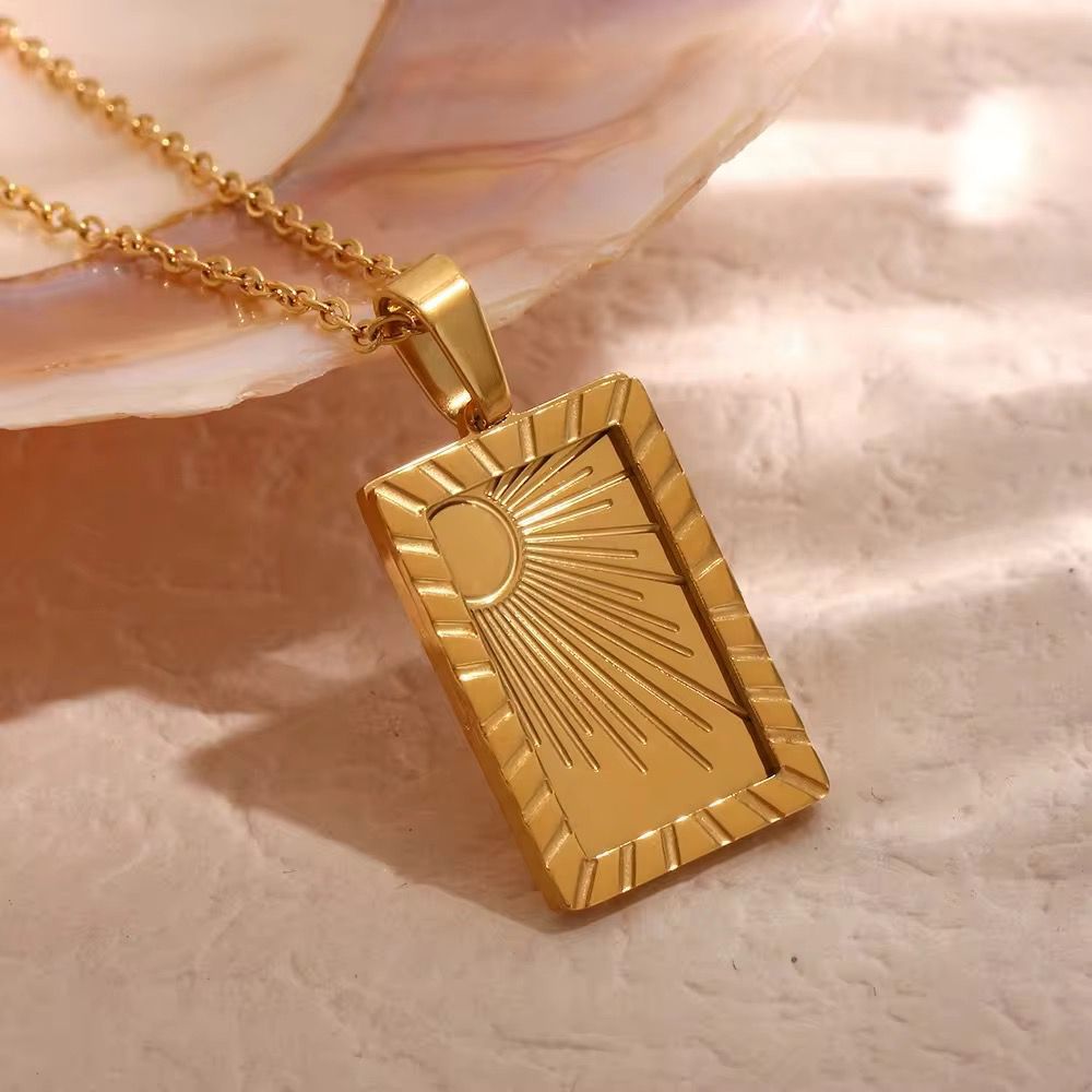 An appealing lifestyle photograph of a model in a full body pose with her hand, highlighting the engraved gold tarot sun card pendant necklace under dramatic lighting against a minimal background.