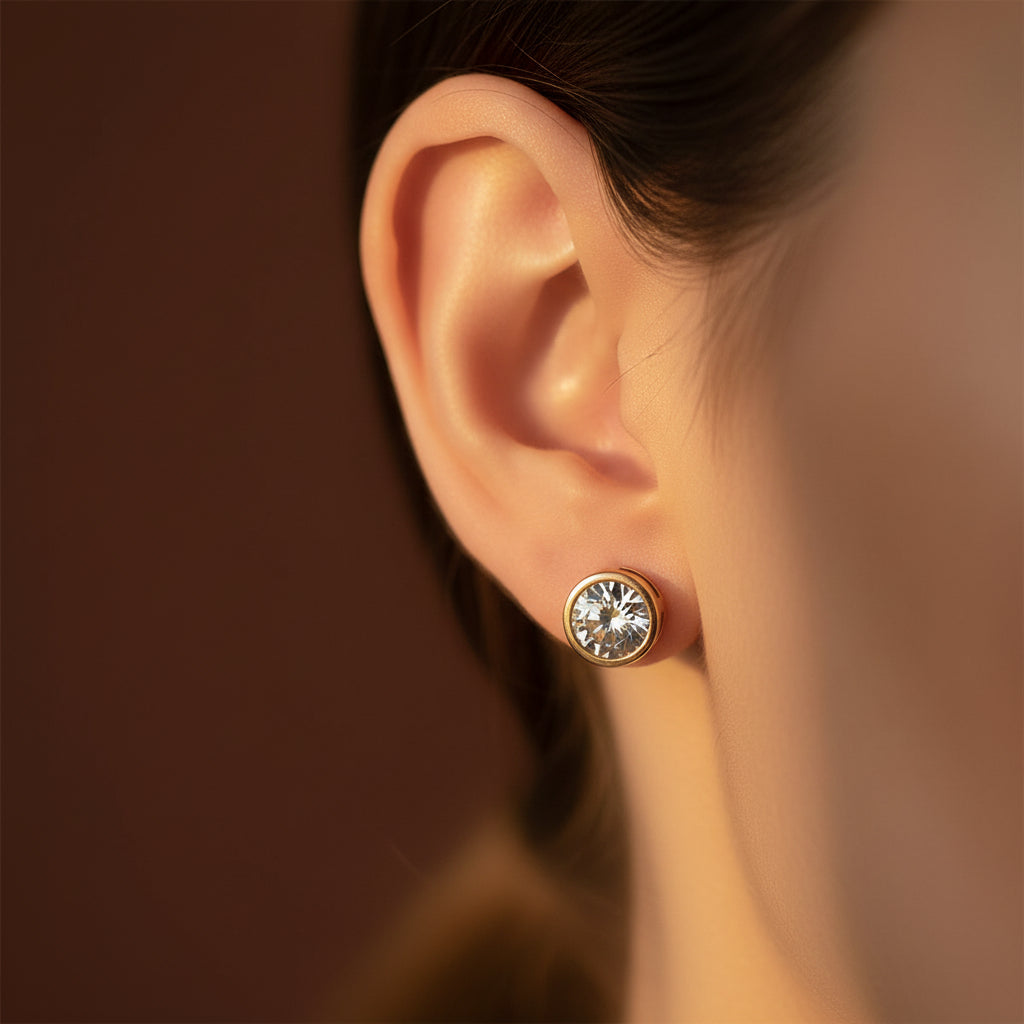 Zoomed-in lifestyle view of a model wearing the gold round crystal bezel stud earrings in warm golden lighting on a rich brown background.