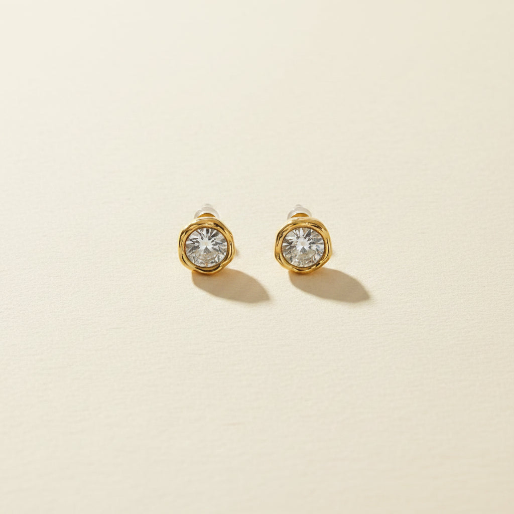 Professional standing catalogue shot of the 18K gold plated textured liquid gold crystal studs with simple shadows on a light cream background.