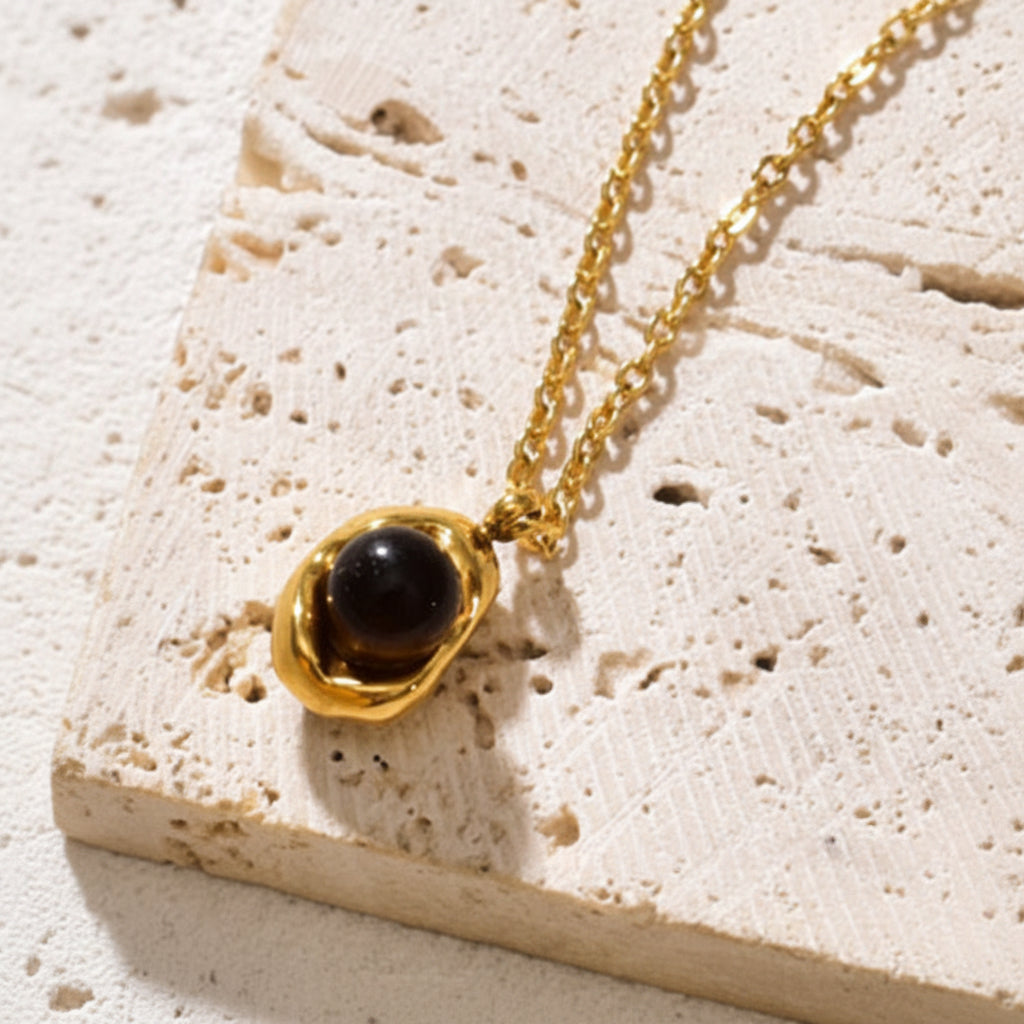 Black stone pendant necklace styled on cream linen with luxury jewellery accessories.