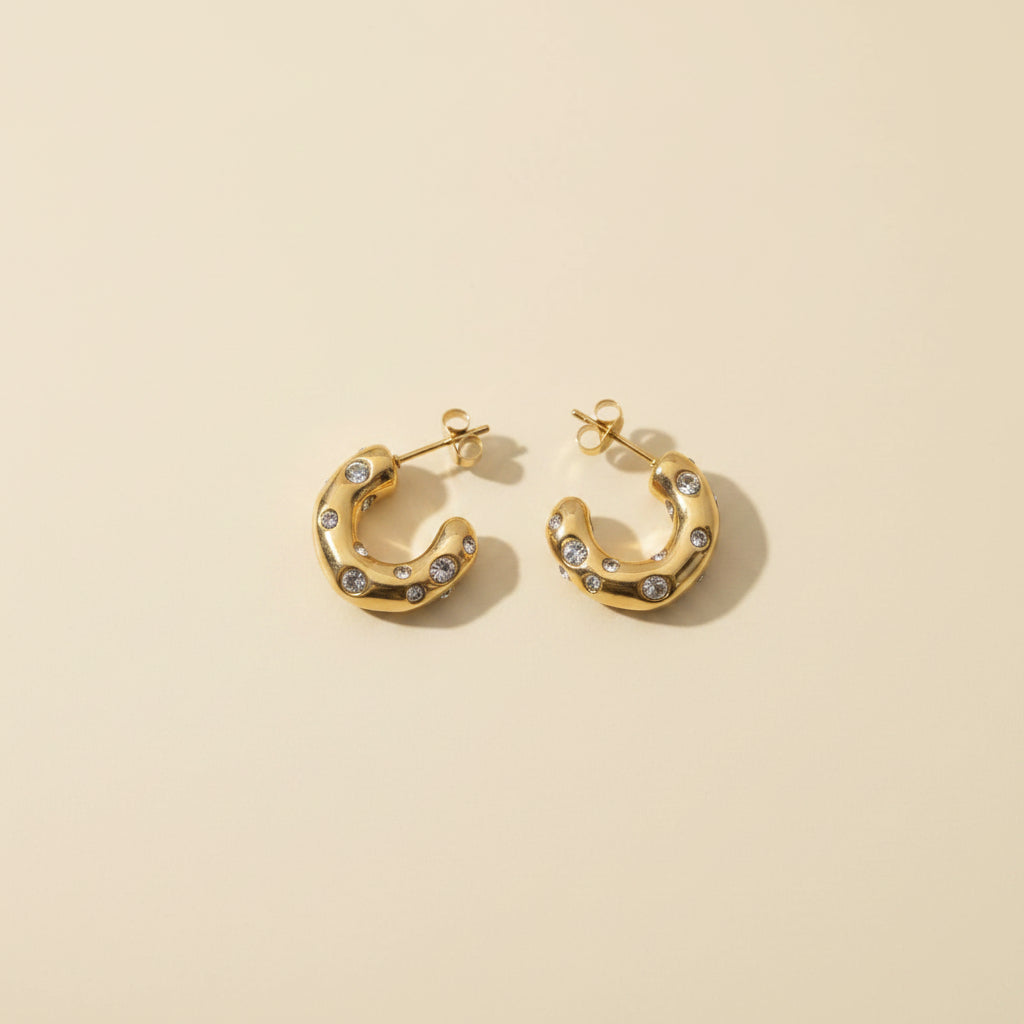 Gold pavé link hoop earrings on a premium #f5f3eb catalogue background.