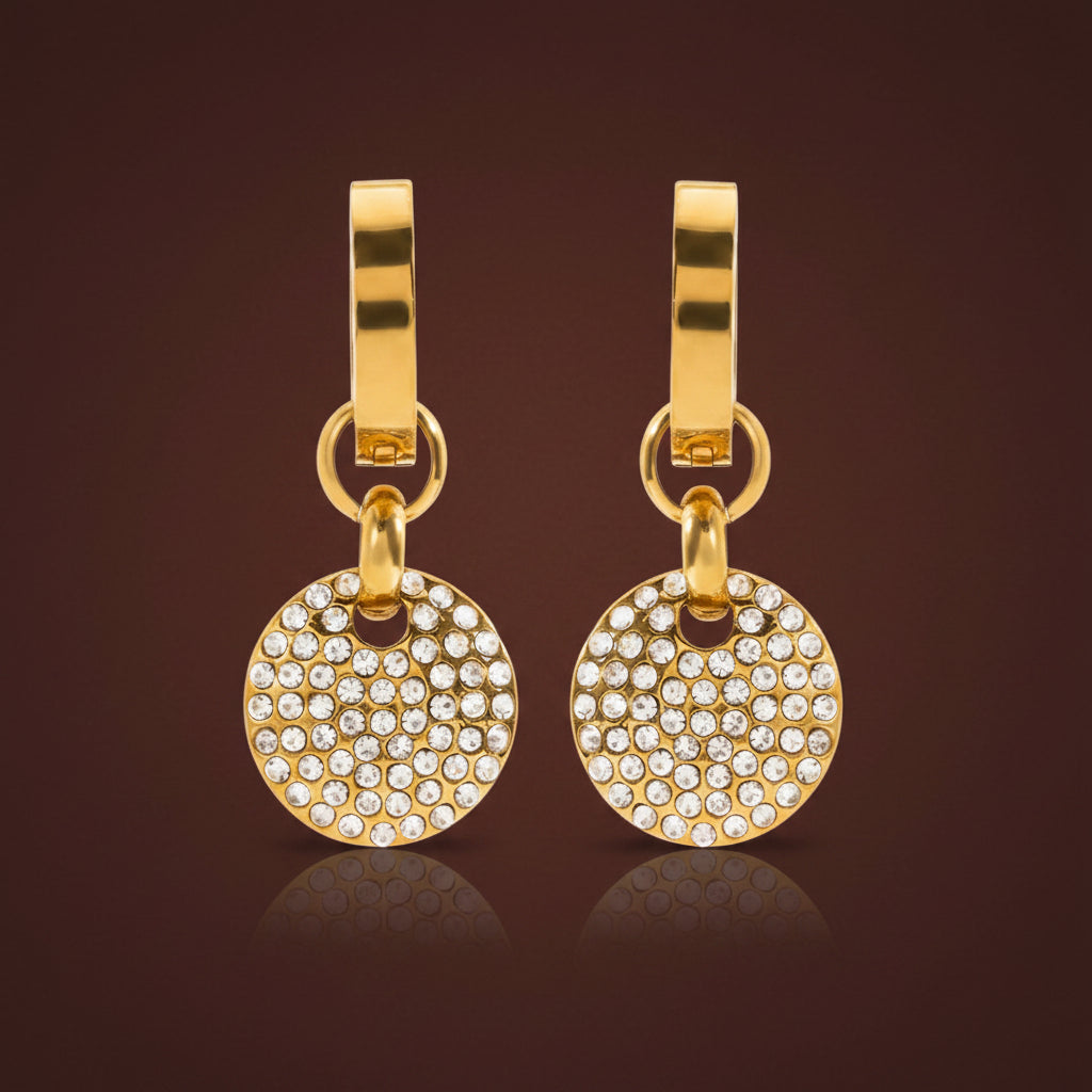 Professional catalogue flat lay of the Aura pavé crystal disc drop earrings in 18K gold plating with soft shadows on a rich brown background.