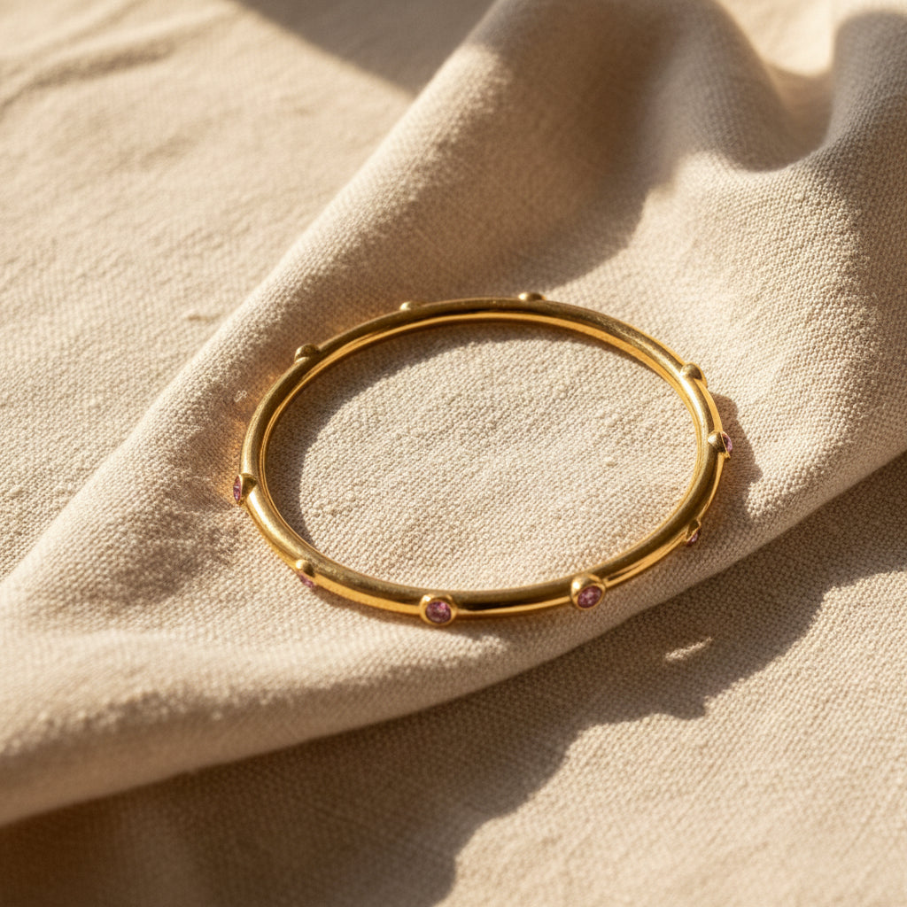 Gold bracelet with pink stones on a white protective surface