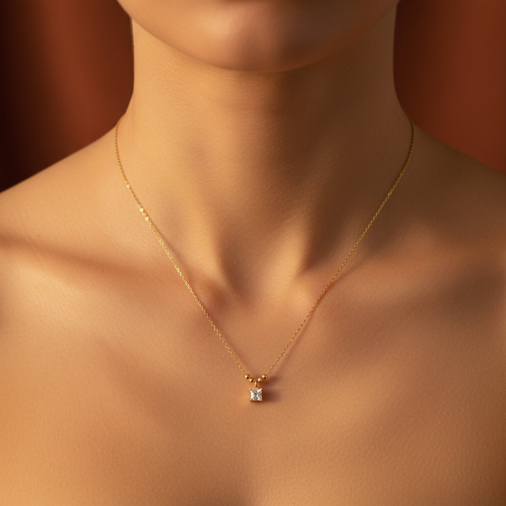 A detailed, realistic photograph focusing on a woman's neck, wearing the 18K gold plated princess-cut square solitaire necklace under warm golden lighting against a solid deep cocoa brown background.