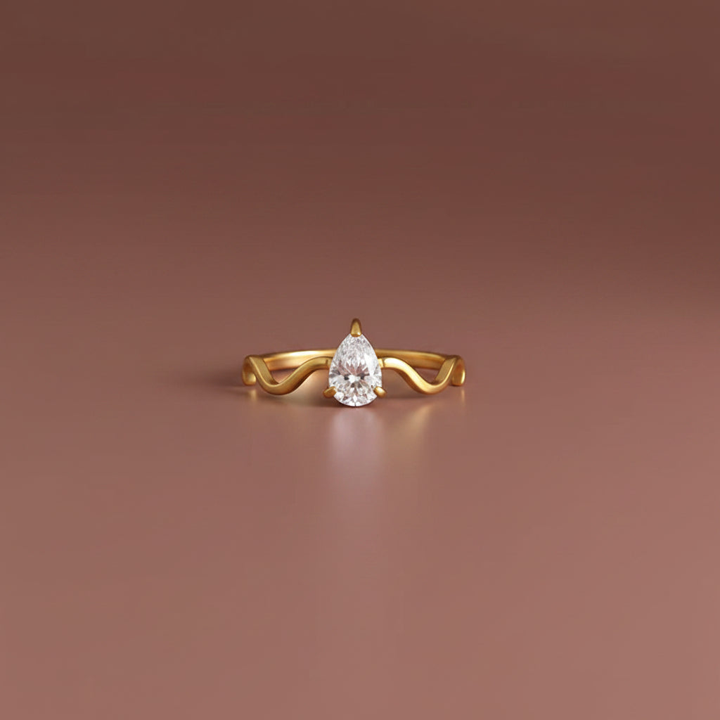 Serena Wave Pear Ring in 18K gold plated stainless steel with pear-cut Cubic Zirconia on a luxury brown catalogue background