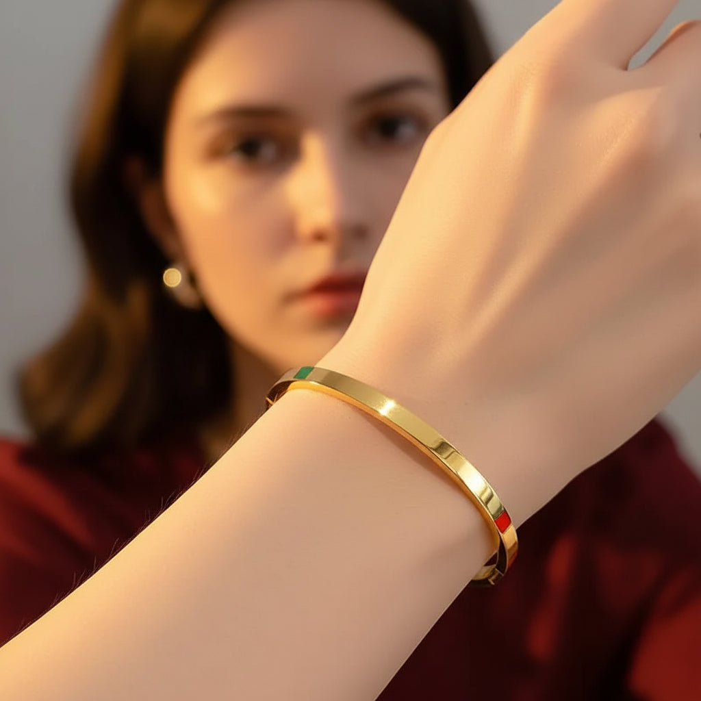 A close-up flat lay photograph focusing tightly on a model's distinctly slender, thin hand and wrist wearing the small plain gold oval kada bangle under warm golden lighting against a deep brown background.