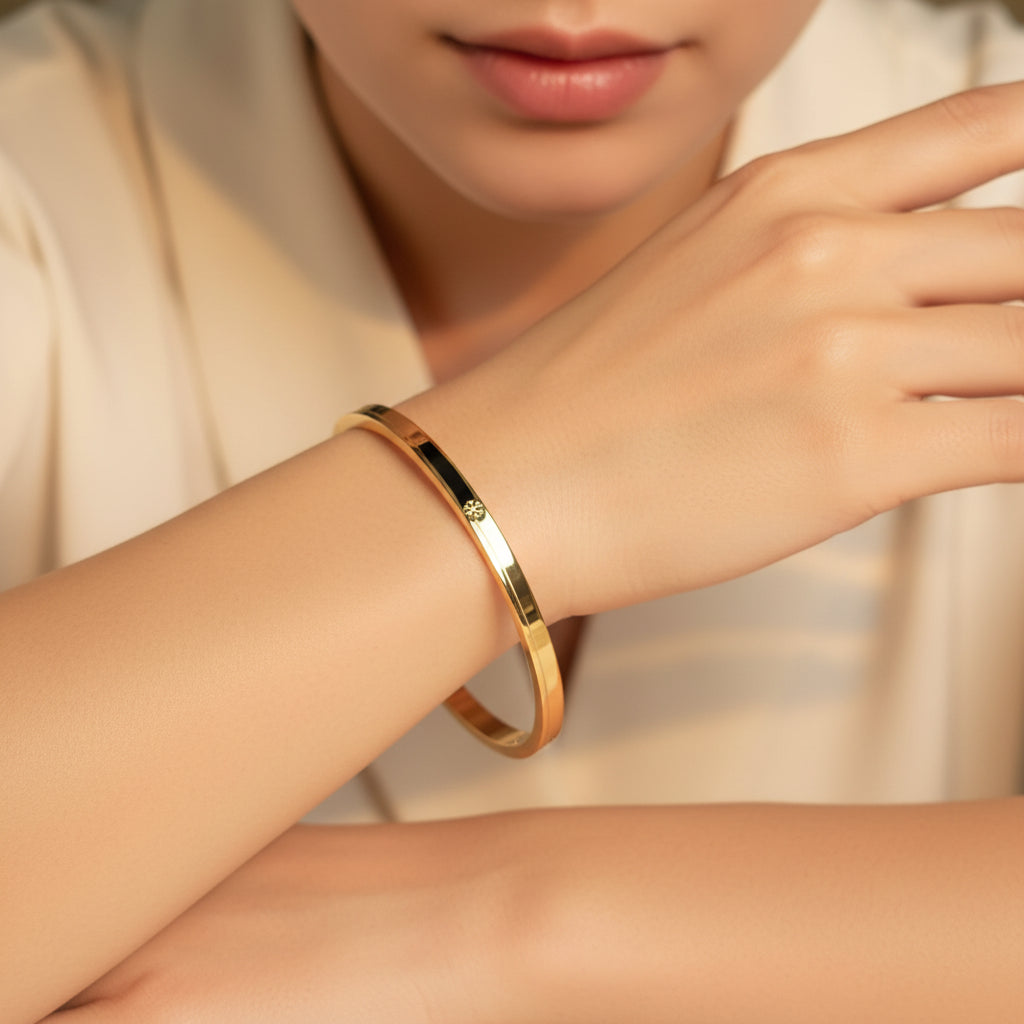 A standing profile photograph of a model (face half visible), showcasing the sleek small size gold snowflake oval bracelet on her thin wrist under warm golden lighting against a cream background.