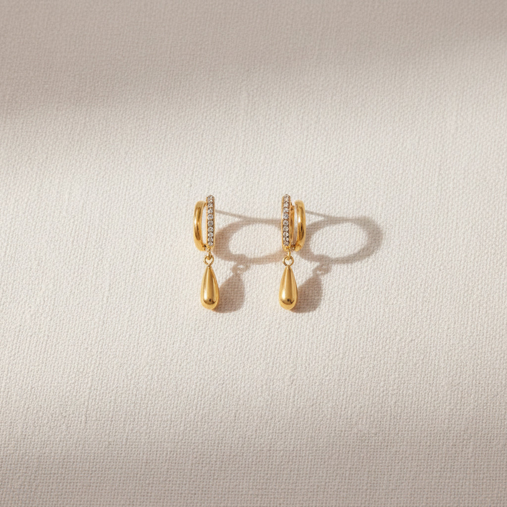 Professional standing catalogue shot of the 18K gold plated layered split-hoop crystal pendant earrings with simple shadows on a light cream background.