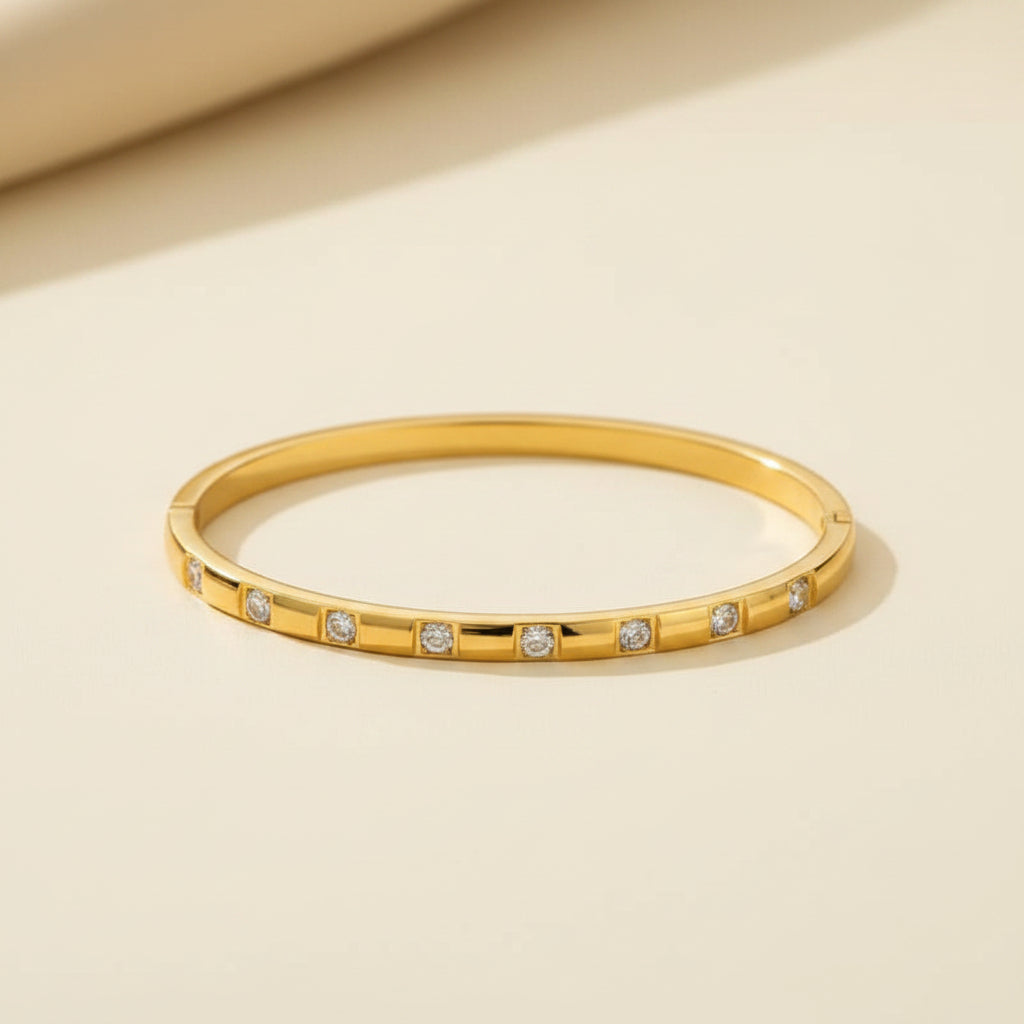 A professional standing catalogue view of the small size gold plated block-station crystal bangle for thin wrists, with clean shadows on a light cream background, as seen in WhatsApp Image 2026-06-18 at 9.28.09 AM.jpeg.